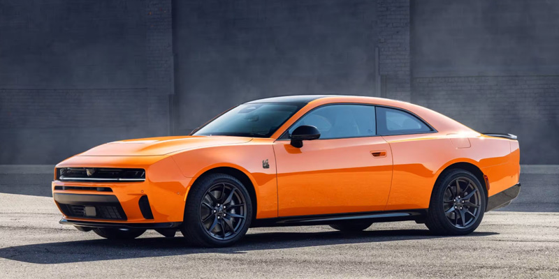 The image features an eye-catching orange Dodge Challenger, showcasing its powerful and muscular design with a sleek, sporty aesthetic set against an industrial backdrop.

