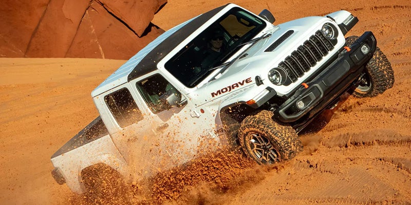 2026 Jeep Gladiator Mojave tackling rugged desert terrain, kicking up sand with its off-road tires.